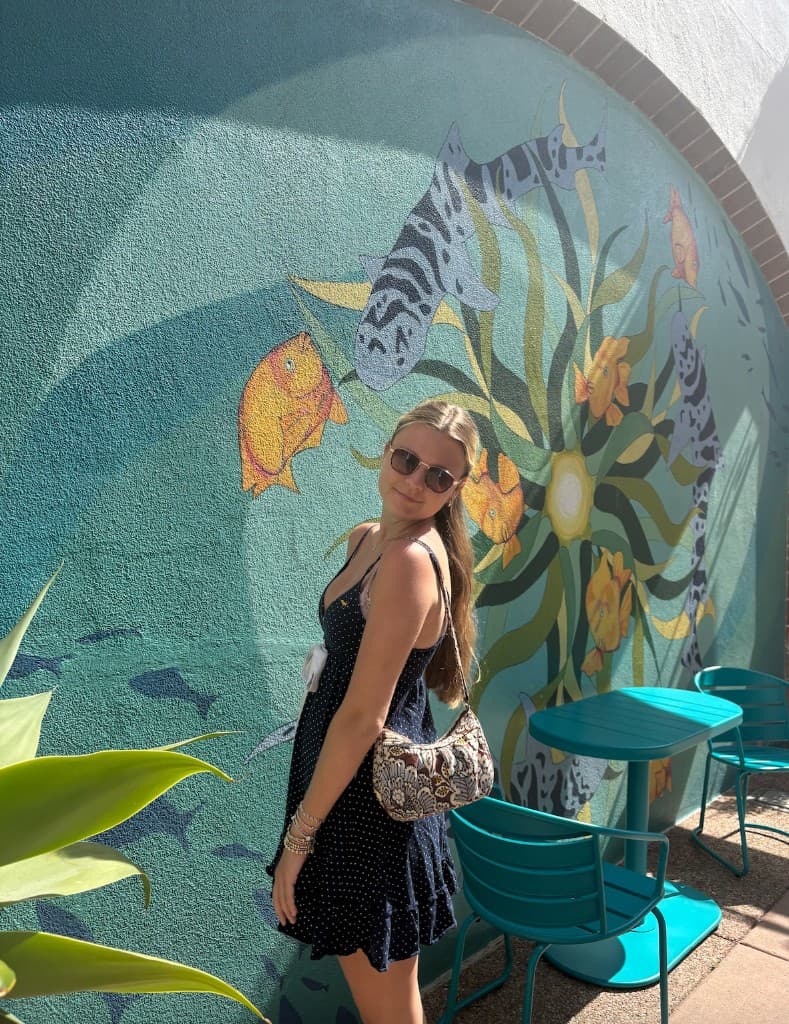 Lily standing in front of a colorful mural on a sunny day
